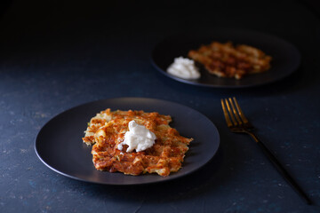 toasted Viennese zucchini waffles with sour cream sauce on two black plates on a dark concrete background.