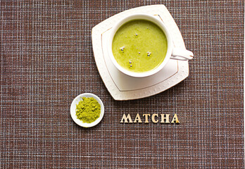 Japanese matcha green tea is poured into a white mug and on a white saucer in powder. Inscription in wooden letters in English. Tea set, invigorating drink, vigor, antioxidant. space for text