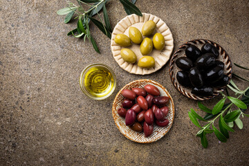 Black and green olives and olive oil in bowls on stone background. Top view with copy space for text.