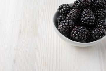 Top view of white bowl with blackberries on white wooden table, horizontal, with copy space