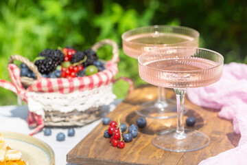 Outdoor summer lifestyle with a gourmet picnic laid out in a garden with berries, pie and pink drink in stylish glasses