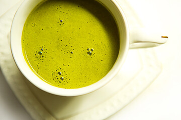 Japanese matcha green tea is poured into a white mug and on a white saucer in powder. Tea set on a textured napkin. Invigorating drink in a cafe, cooking, cheerfulness, antioxidant. space for text