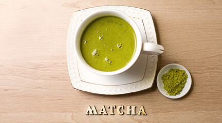 Japanese matcha green tea is poured into a white mug and on a white saucer in powder. Inscription in wooden letters in English. Tea set, invigorating drink, vigor, antioxidant. space for text