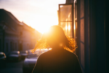 Silhouette of a woman with hair in the rays of the setting sun on the street during sunset - Powered by Adobe