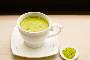 Japanese matcha green tea is poured into a white mug and on a white saucer in powder. Tea set on a textured napkin. Invigorating drink in a cafe, cooking, cheerfulness, antioxidant. space for text