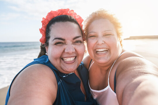 Curvy women friends taking selfie on the beach with sunset in background - Happy plus size body female having fun together - Curves and confident concept