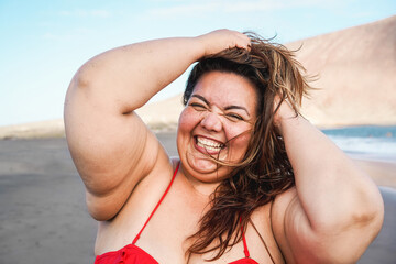 Happy curvy woman smiling on camera wearing bikini with beach in background - Plus size person and...