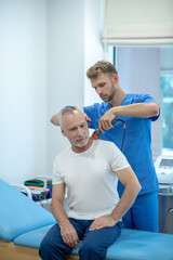 Bearded doctor performing ultrasound neck treatment on mature patient