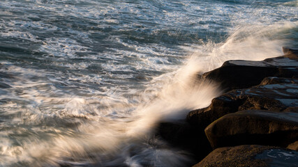 Waves crashing against the rocks at sunset