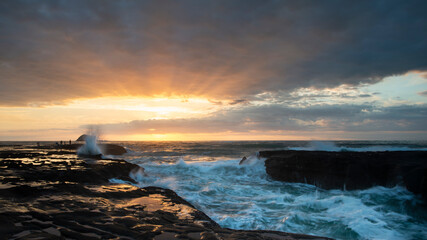 Fototapeta premium Sunset at Muriwai beach with splashing waves against the rocks