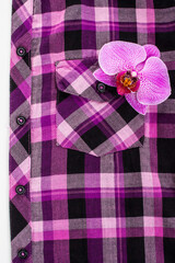 Fashion concept. Purple checkered shirt and pink orchid. Top view.