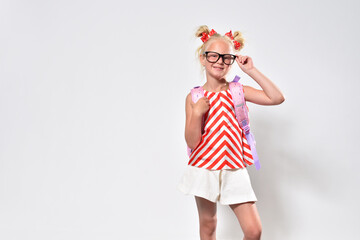 Schoolgirl in glasses with a backpack smiling on a gray background