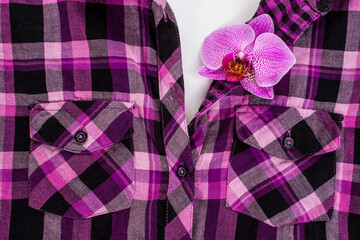 Fashion concept. Purple checkered shirt and pink orchid. Top view.