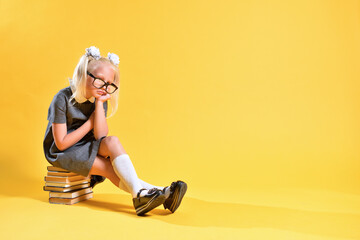 A girl from elementary school has lost interest in studying and sits sad on a stack of books
