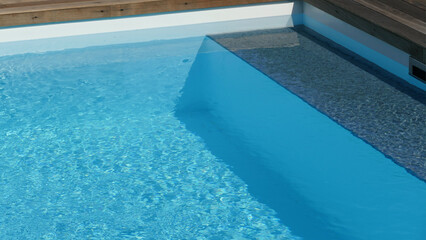 Schöner blauer Pool mit einer Umrandung aus Holz und einer kleinen Bank für die Füße im Wasser
