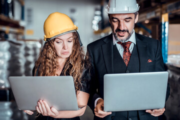 Engineer woman and businessman wearing a hardhat standing cargo at goods warehouse and check for control loading from Cargo freight ship for import and export by report on laptop. Teamwork concept