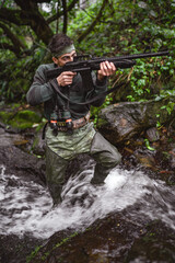 Fototapeta premium Soldier or revolutionary member or hunter in camouflage in the stream aiming the gun in his hand, hunter concept