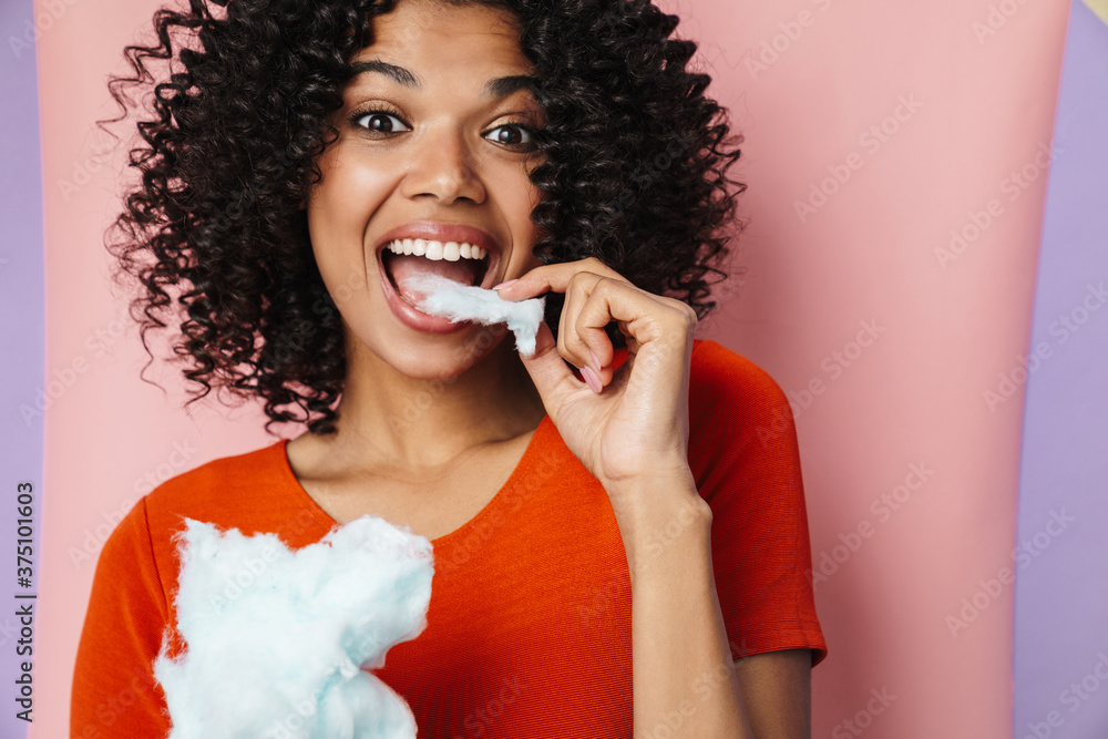 Wall mural Image of joyful african american woman smiling while eating cotton candy