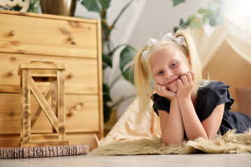 Cute little girl child with a smile in her room on the floor next to the tent wigwam © pridannikov