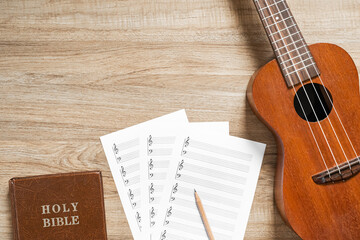Top view of ukulele with blank stave pad bar for music notes and Holy Bible on wood texture...