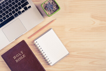 Top view of Holy Bible, laptop, notebook, and pencil on wooden background