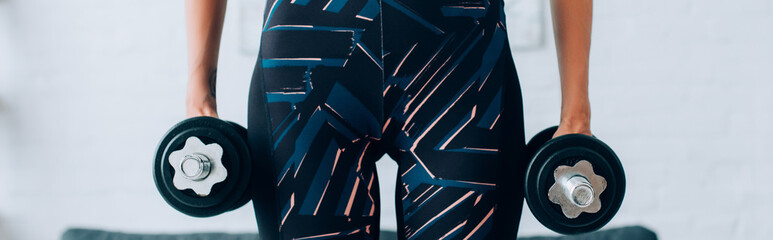 Panoramic shot of sportswoman holding dumbbells at home