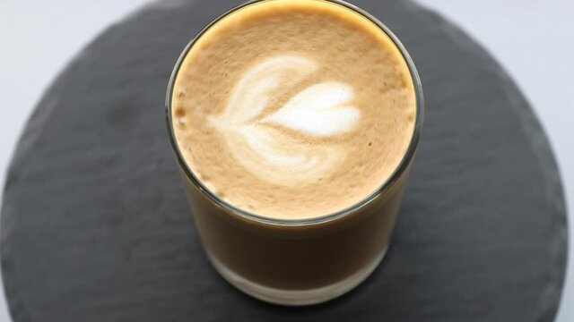 transparent coffee glass with rosetta latte art rotating on a black stone plate, template for summer drink menu of cafe and restaurant
