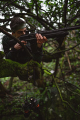 Soldier or revolutionary member or hunter in camouflage on the tree aiming the gun in his hand,...