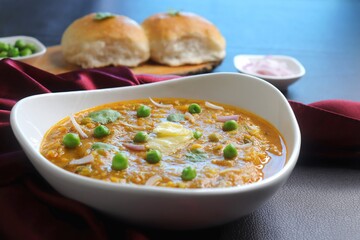 Indian Mumbai Street style Pav Bhaji, garnished with peas, raw onions, coriander, and Butter. Spicy thick curry made of out mixed vegetables served with paav over black background with copy space. 