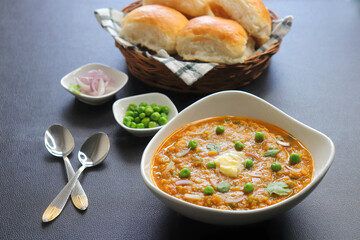 Indian Mumbai Street style Pav Bhaji, garnished with peas, raw onions, coriander, and Butter. Spicy thick curry made of out mixed vegetables served with paav over black background with copy space. 