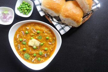 Indian Mumbai Street style Pav Bhaji, garnished with peas, raw onions, coriander, and Butter. Spicy thick curry made of out mixed vegetables served with paav over black background with copy space. 