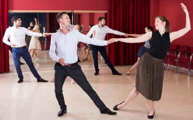 Positive people dancing lindy hop in pairs in dance hall