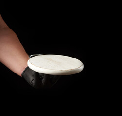 male hand in black latex glove holds round empty white wooden pizza board