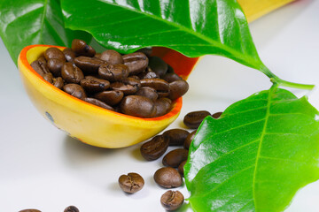Coffee beans in a wooden spoon on a white background.