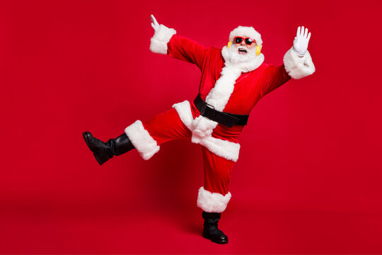 Full length photo of pensioner old man grey beard hands up open mouth entartainer wear santa costume x-mas coat belt sunglass headwear earphones black boots isolated red color background