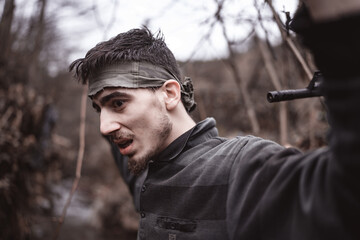 Revolutionary member or soldier man in the forest with a gun imposed on his head raises his hostage hands and surrenders