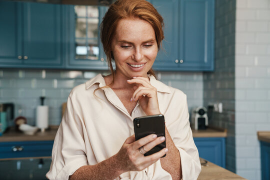 Image of smiling redhead woman using cellphone while standing