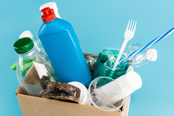 plastic rubbish and rubber gloves in cardboard box on blue background