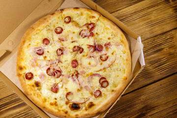 Delicious fresh pizza in cardboard box on a wooden table. Top view. Concept for home delivery of food, fast food, delivery of pizza