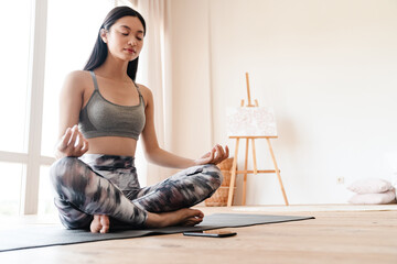 Image of focused asian girl using mobile phone while meditating