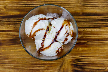 Vanilla ice cream with chocolate topping in glass bowl on a wooden table. Top view