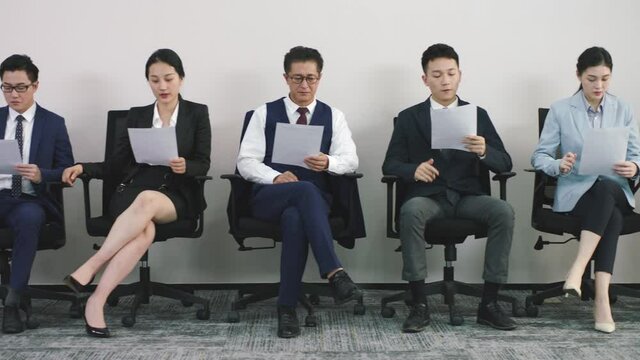 group asian corporate executives job applicants sitting in lined up chairs waiting for interview