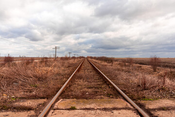 Obraz premium View of an empty railway road outside the city. Telegraph poles. Clouds in the sky.