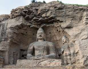 Iconic seated Buddha statue and smaller standing Buddha on right in Cave 20 at Yungang Grottoes, Datong, Shanxi, China. Constructed from 5th century. UNESCO World Heritage.