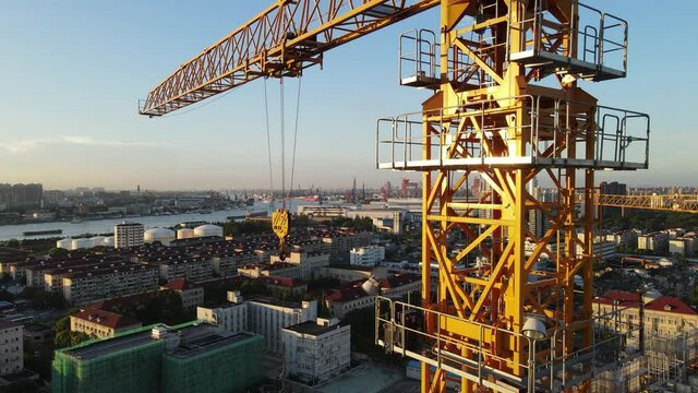 Drone point of view moving up around crane tower in construction site sunset. Close up view of the crane tower lifting material in building site. Industry construction concept footage Shanghai China