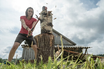 Independent woman choping wood for the winter with a large steel ax in the village, against the...