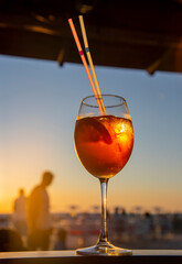 A glass of aperol cocktail stands against the sunset sky.