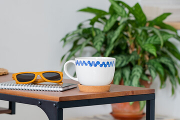 a white mug with a blue pattern, a Notepad and sunglasses on a brown wooden table on a white background. Business lunch. Scandinavian style.