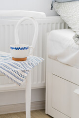 Bedside table with a white mug next to the white bed. Scandinavian style. White background