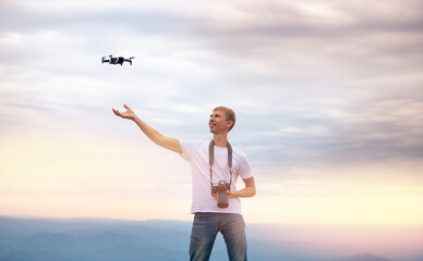 Happy man Photographer with camera controls drone, carries out quadcopter landing on hand, sunset